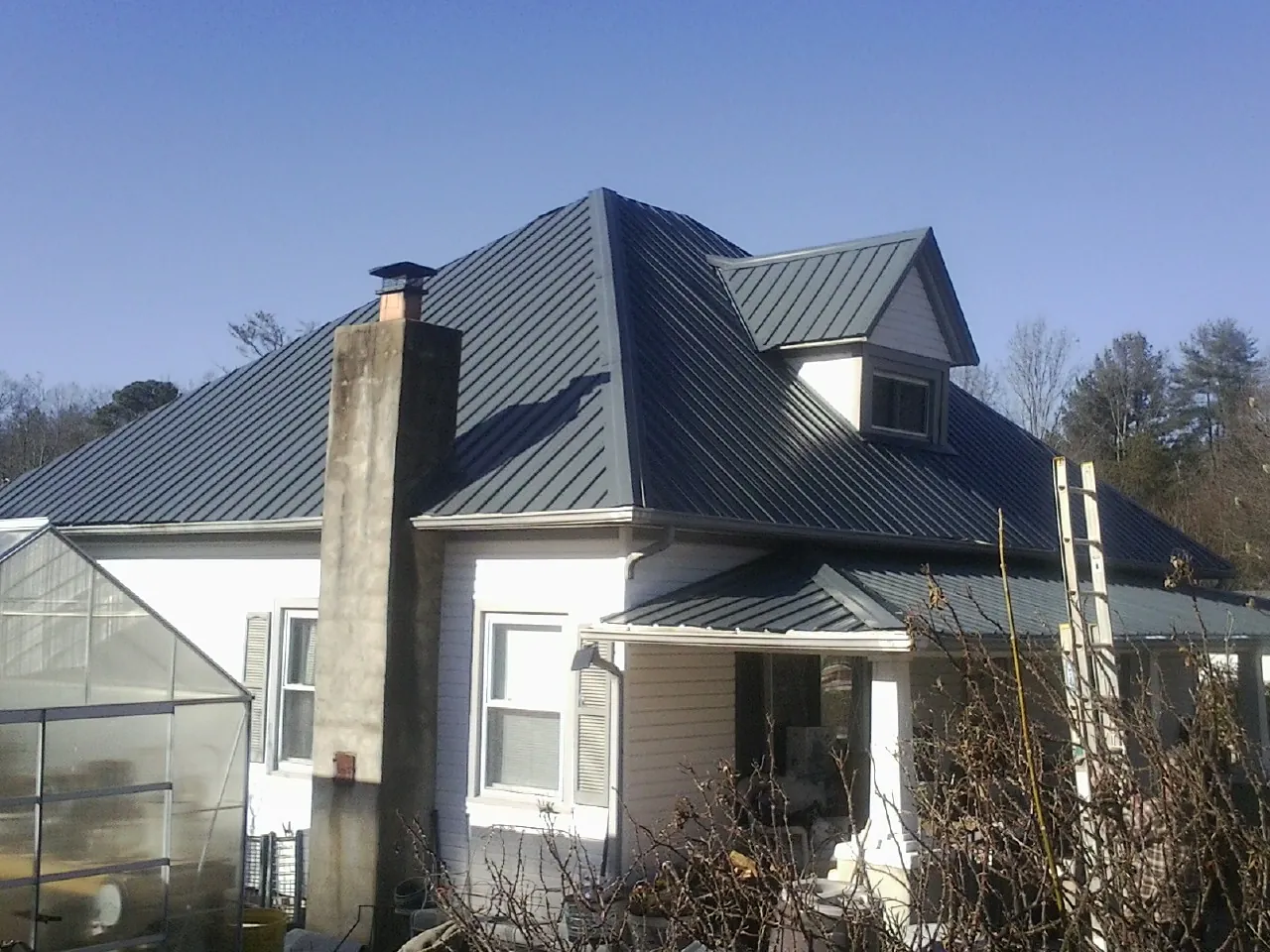 Dark blue standing seam metal roof on a white farmhouse with dormer — Slate & Tile Roof Repair by Roofing Brothers in Saint Joe
