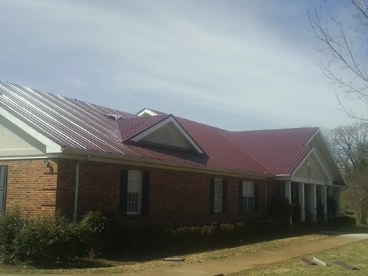 Red metal roof with gabled entries on a long brick building, from a Hail Damage Roof Repair job in Saint Joe