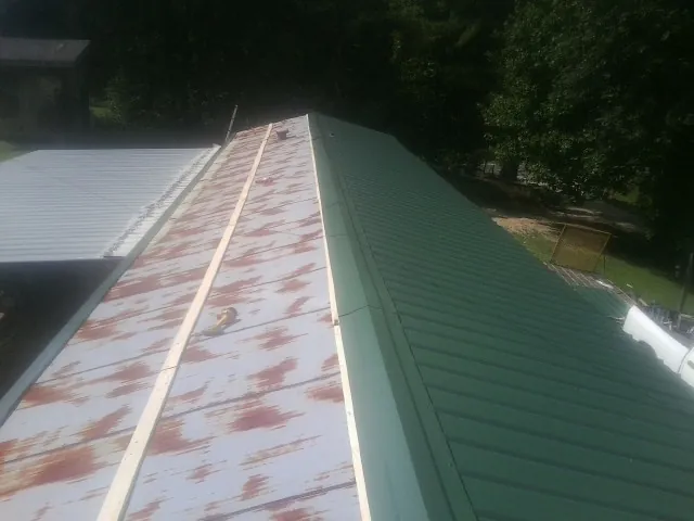 Old rusted panels beside newly installed green metal roofing — Wind Damage Roof Repair by Roofing Brothers in Saint Joe