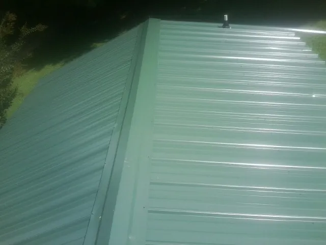 New green metal panels meeting at the ridge of a roof — Flat Roof Repair work by our crew in Saint Joe