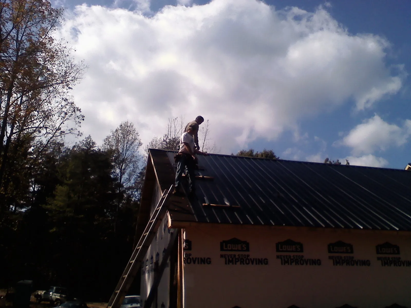 Roofer fastening dark metal panels high against a cloudy sky, from a Roof Inspection job in Saint Joe