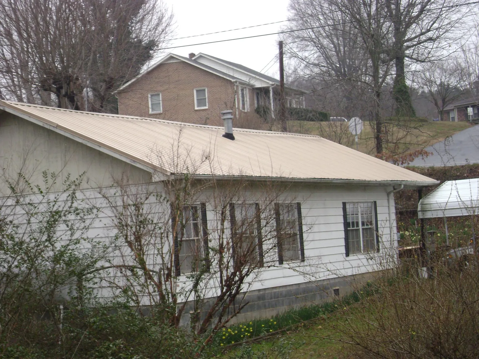Tan metal roof on a white sided house set into a hillside — Commercial Roofing by Roofing Brothers in Saint Joe