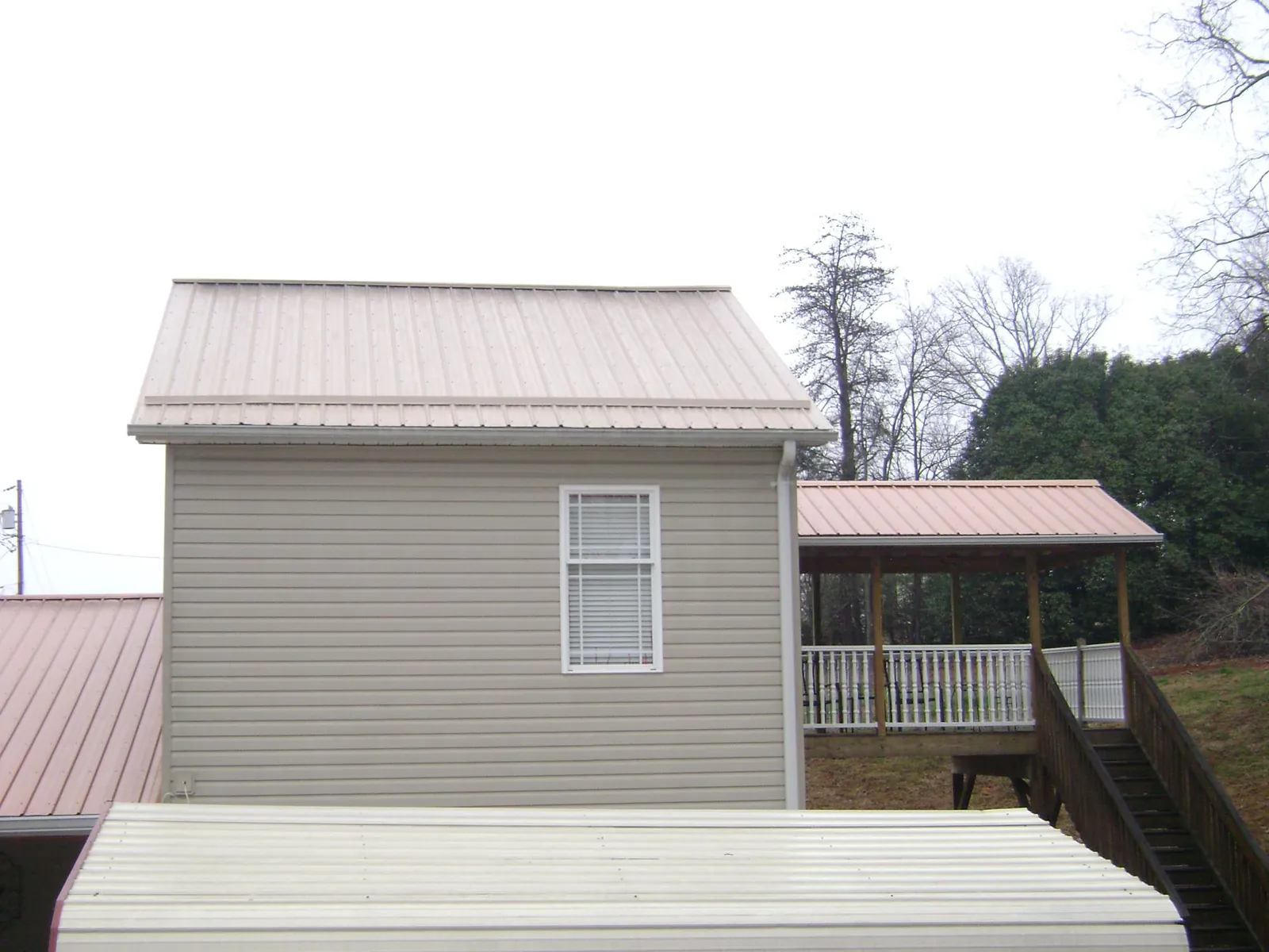 Tan metal roofs on a two story addition and attached porch, from a Roof Replacement job in Saint Joe